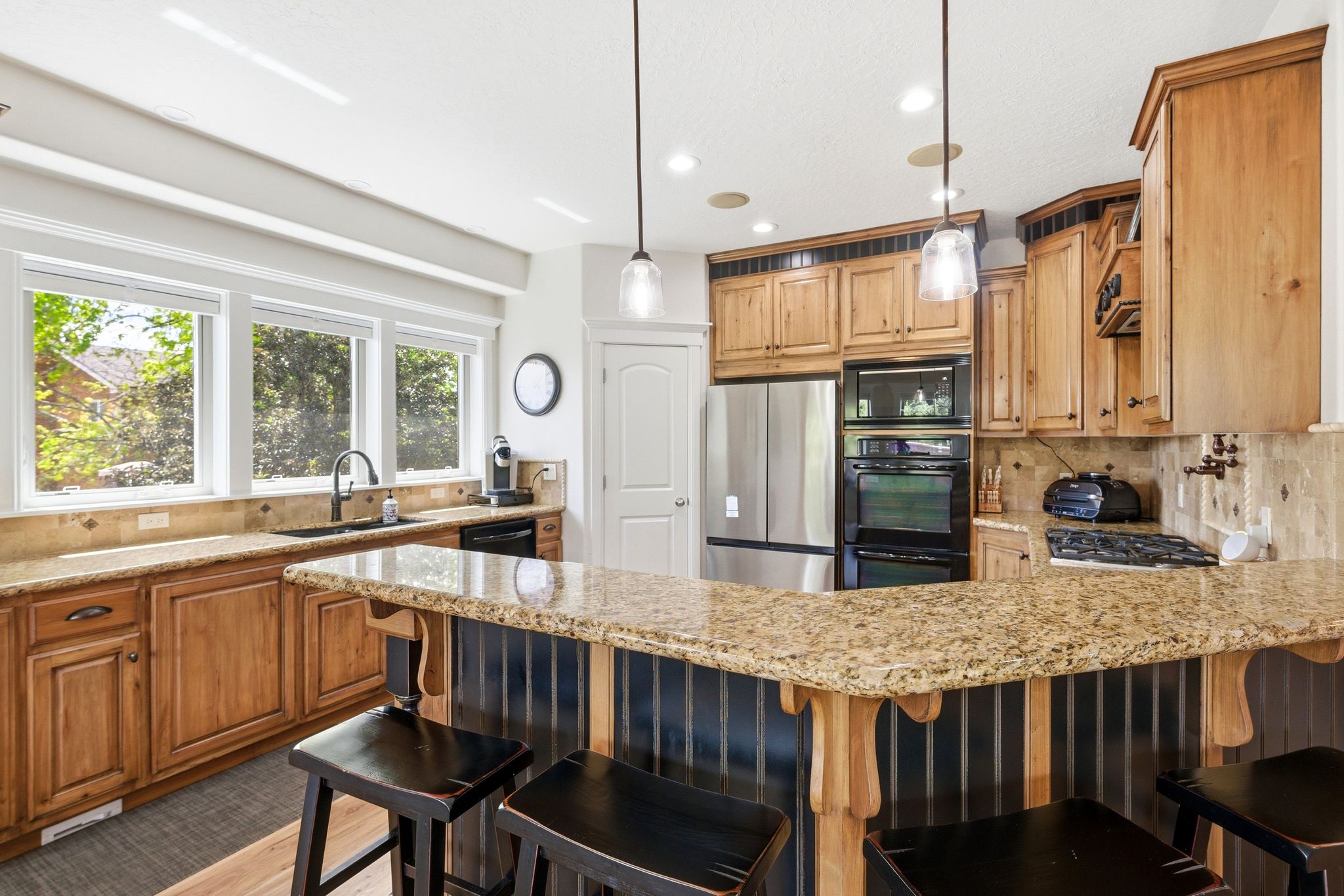 Kitchen featuring a kitchen breakfast bar, backsplash, black appliances, light stone counters, and decorative light fixtures