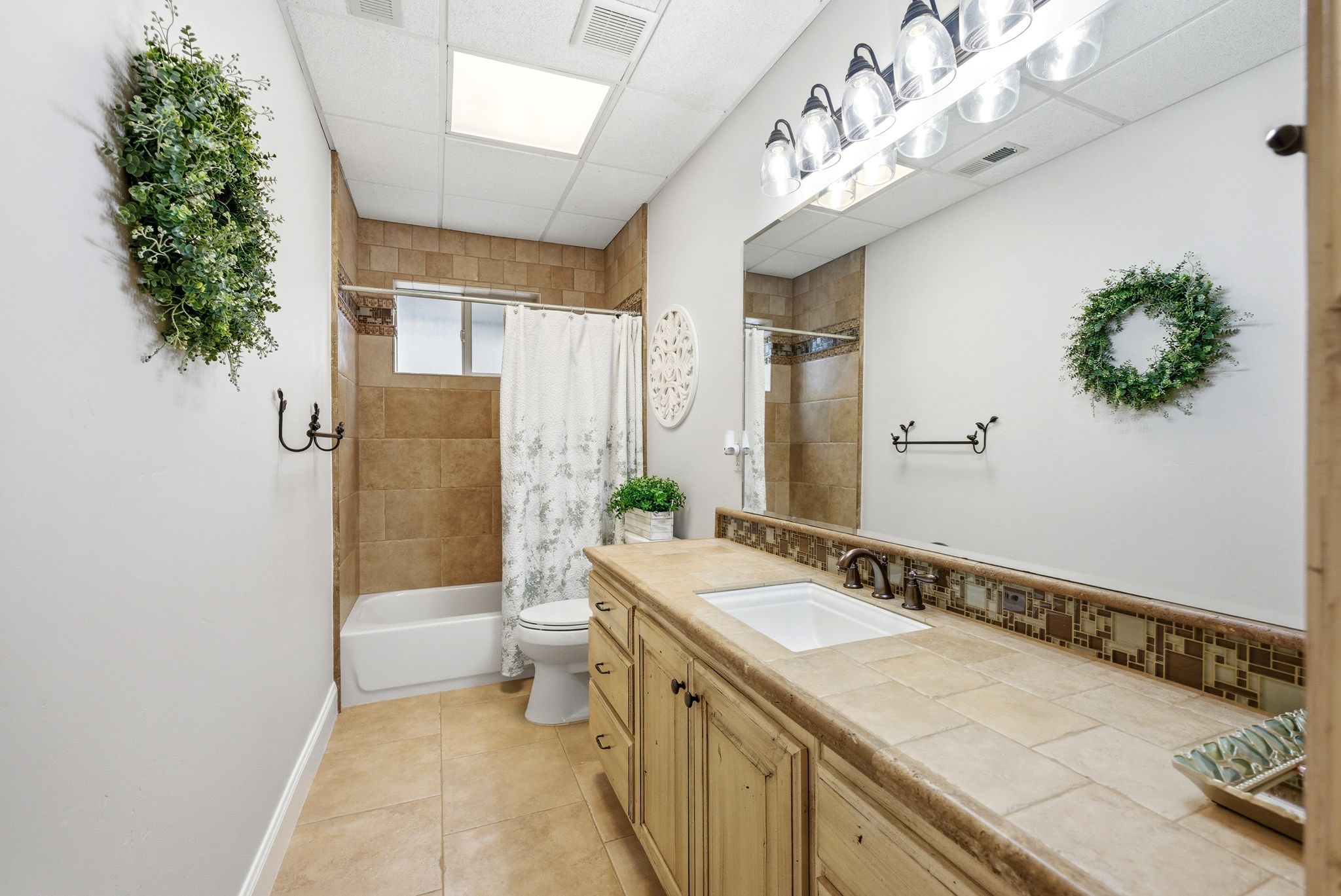 Full bathroom with vanity, shower / bath combo with shower curtain, a drop ceiling, and light tile patterned floors