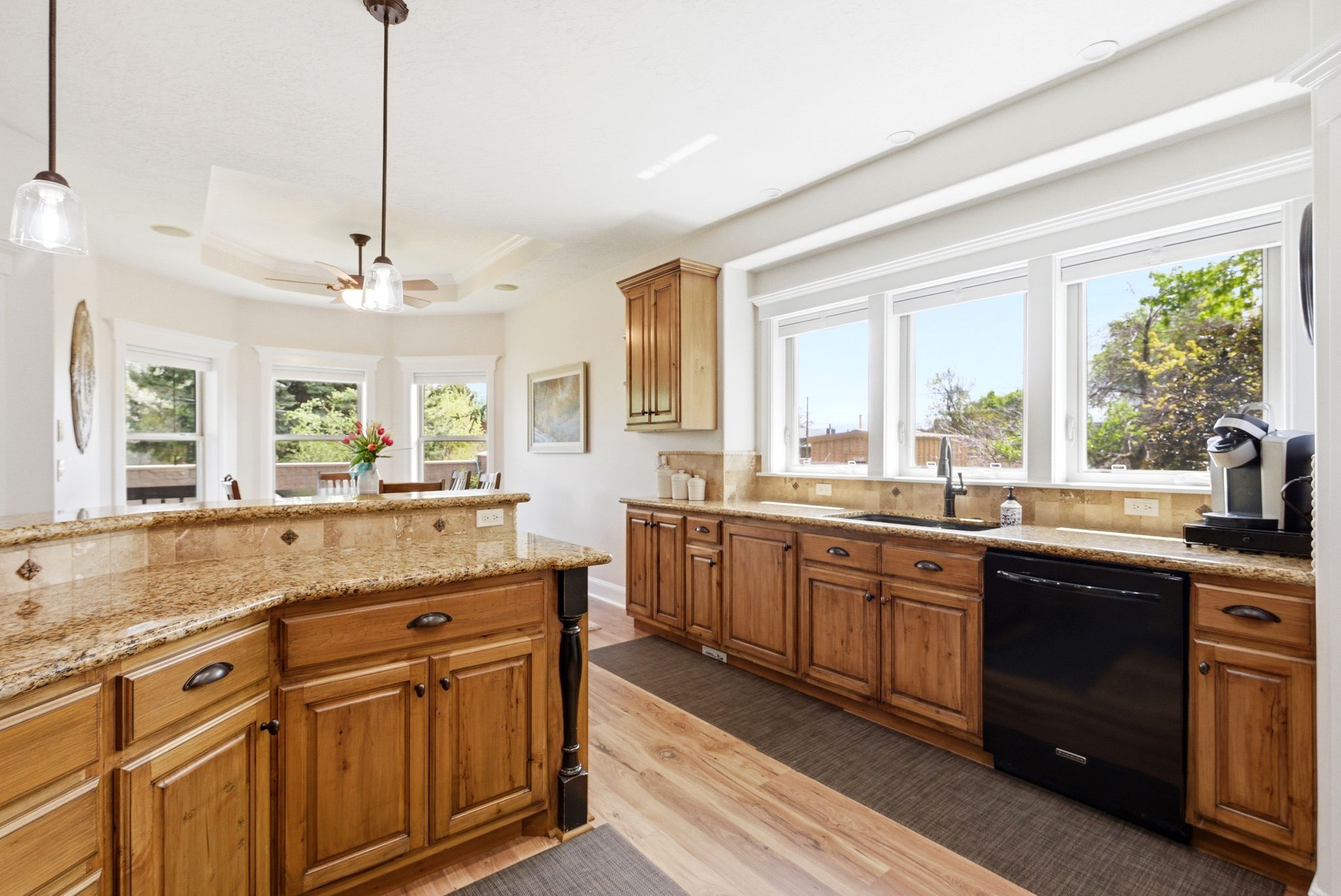 Kitchen featuring wood finish cabinetry, light stone countertops, light wood-style flooring, black dishwasher, and a raised ceiling
