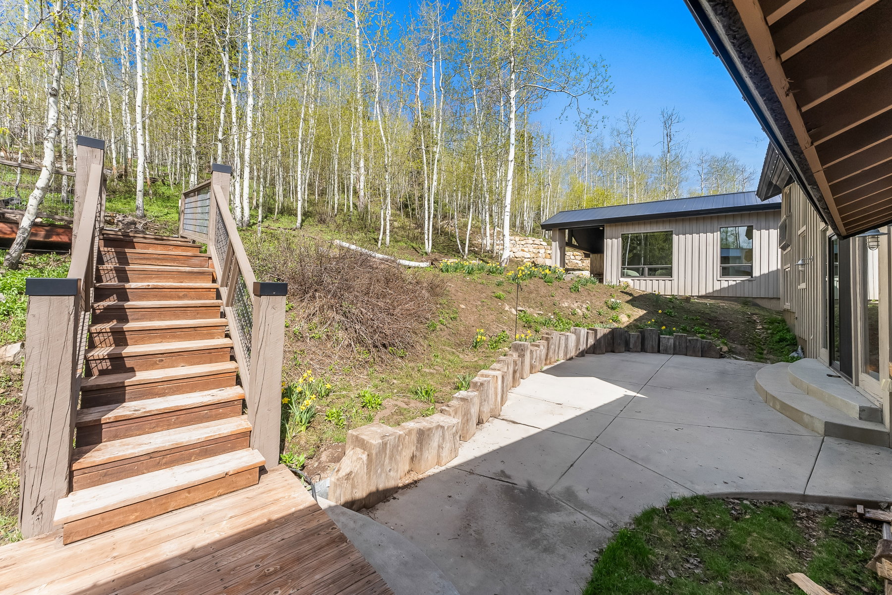 Sloped grounds featuring a multi-level concrete patio, timber retaining walls, and a wood staircase with cable railing