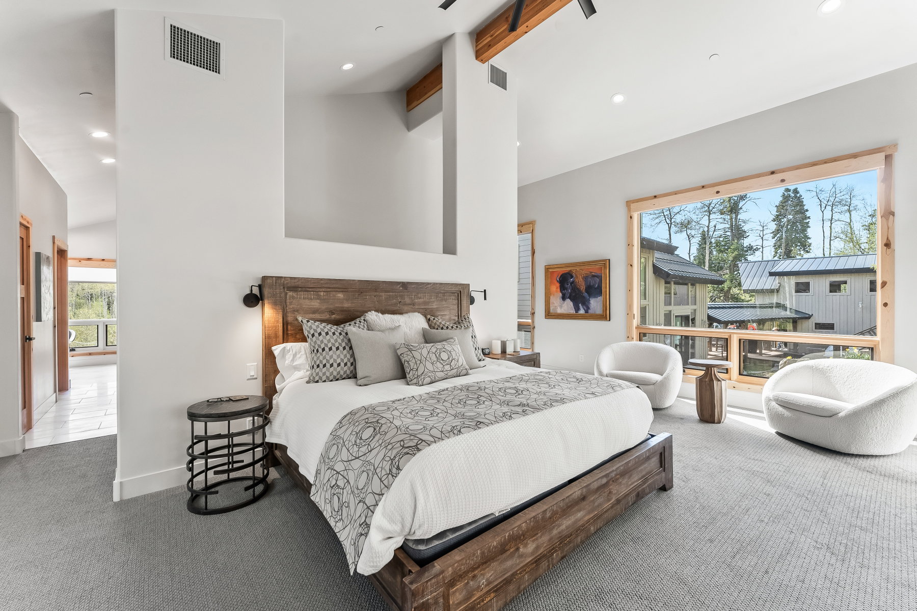 Spacious bedroom featuring a large window with natural wood trim, light gray carpeting, and a rustic wood-finish bed frame