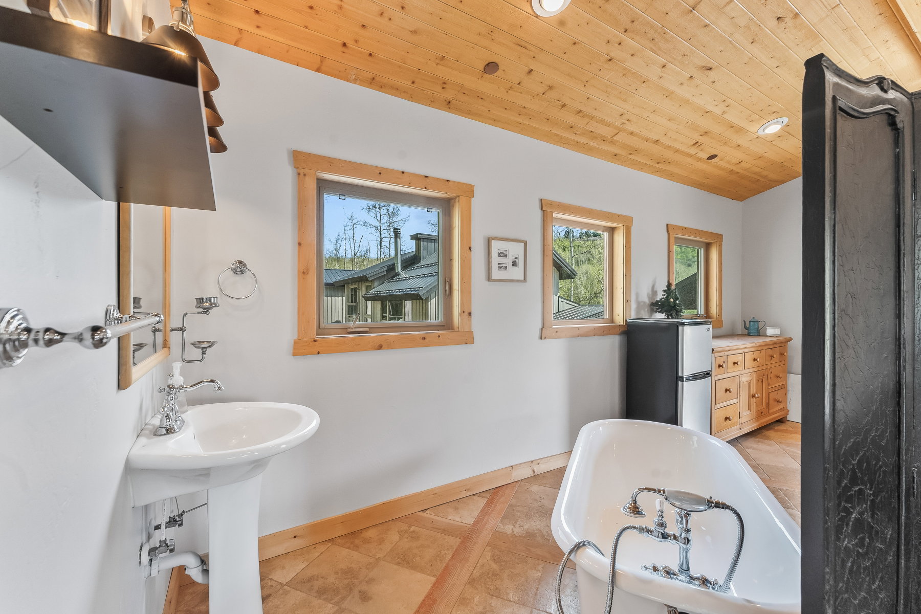 Bathroom featuring a pedestal sink, freestanding tub with chrome fixtures, and a natural wood plank ceiling