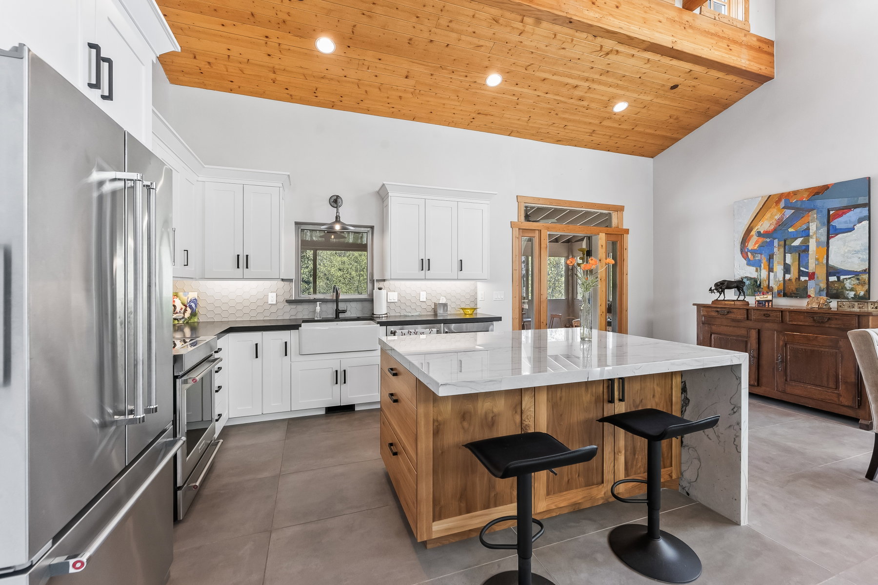Kitchen featuring a large center island with a waterfall-edge countertop, white shaker-style cabinetry, stainless steel appliances, and wood-finish vaulted ceilings