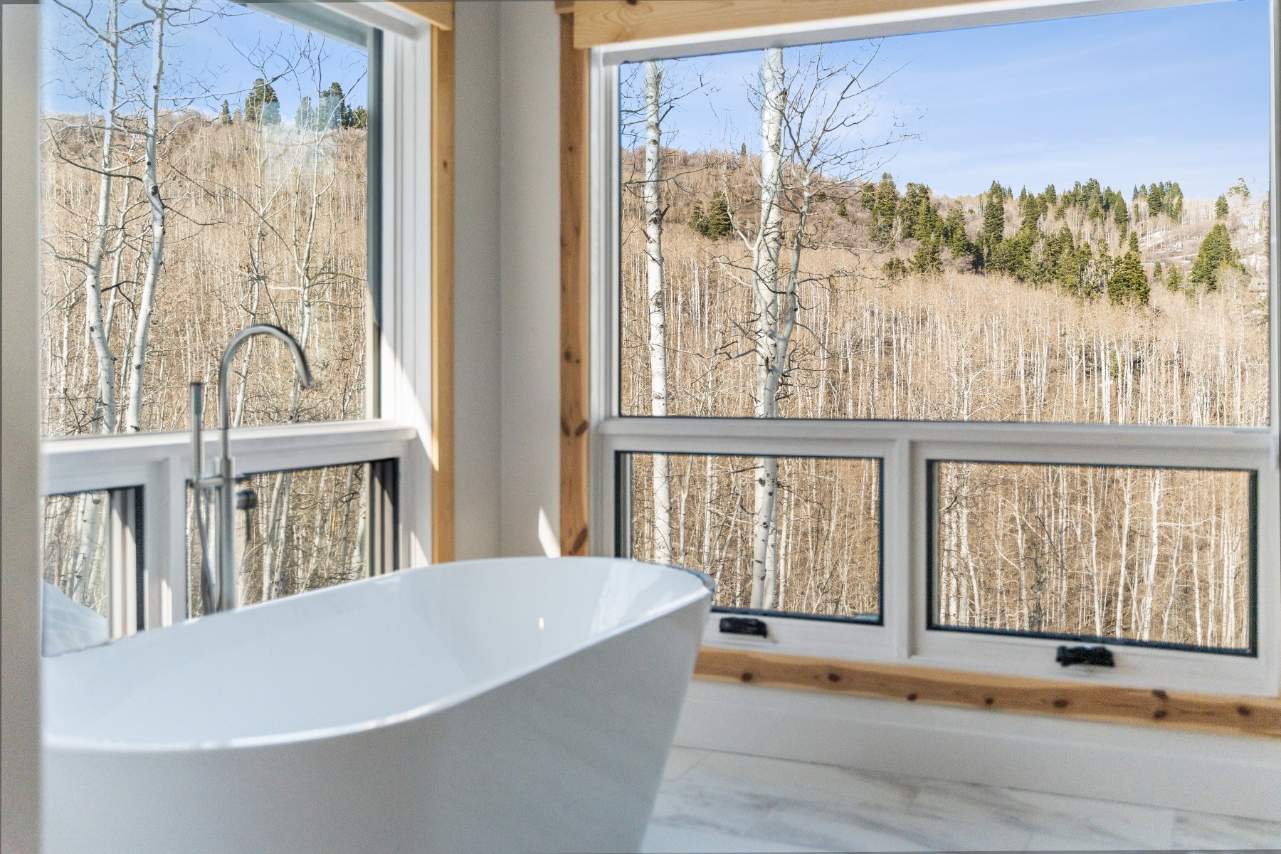 Freestanding soaking tub with a floor-mounted chrome faucet, set against expansive windows with natural wood trim
