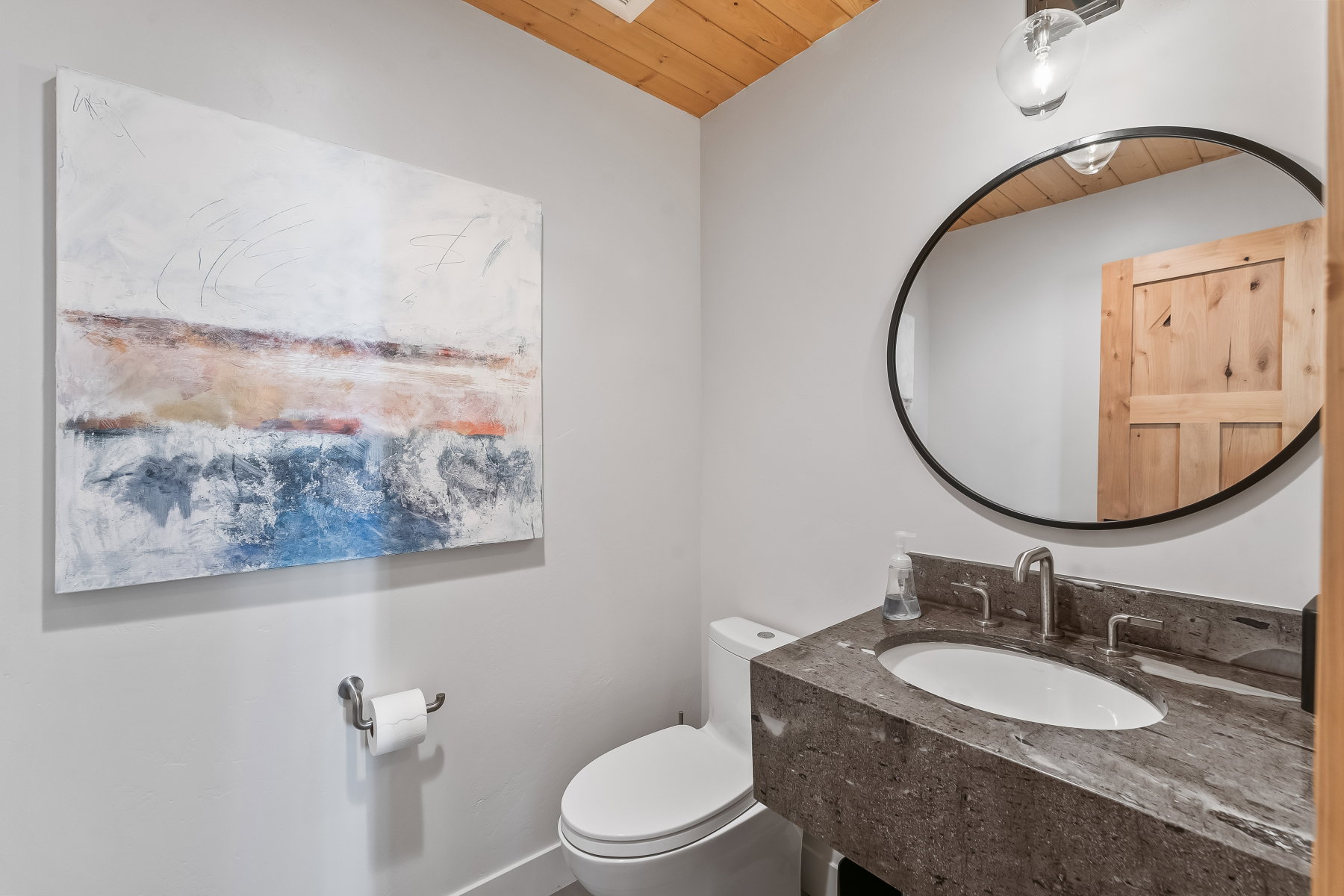 Powder room featuring a wood-paneled ceiling, a dark stone vanity with an undermount sink and brushed nickel faucet, and an oval mirror with a black frame