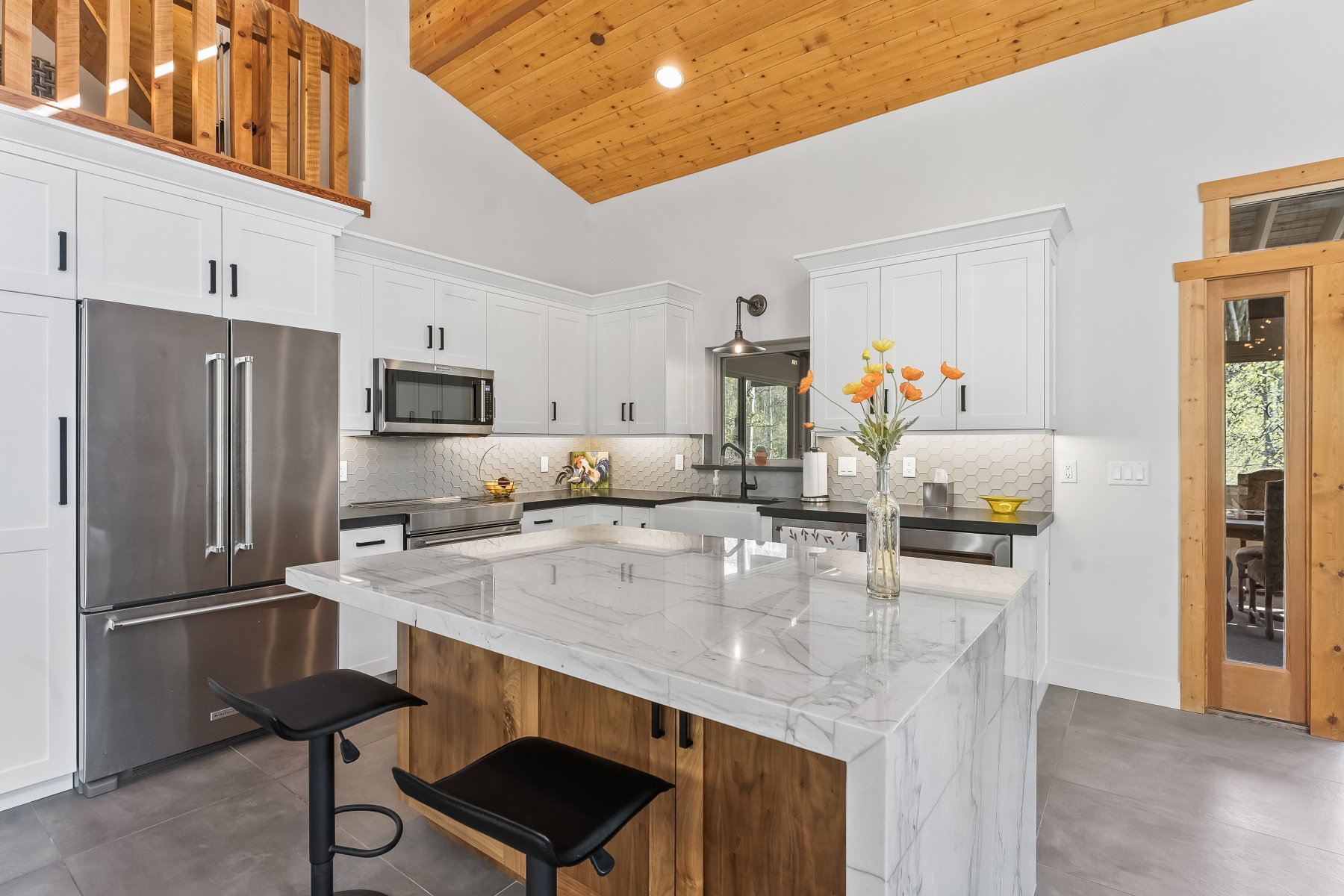 Kitchen featuring a large island with a waterfall countertop, white shaker cabinetry, stainless steel appliances, a honeycomb tile backsplash, and wood-finish flooring