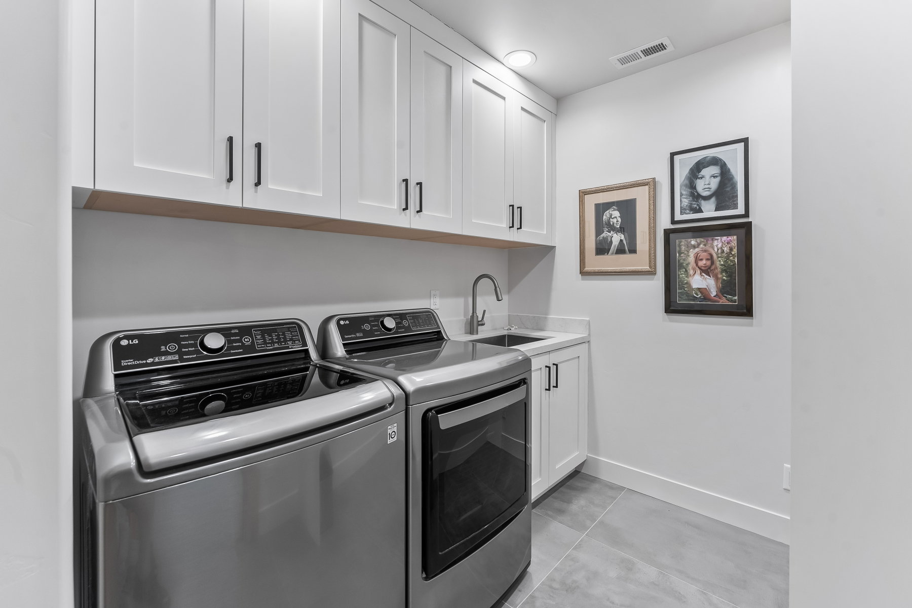 Dedicated laundry space featuring white shaker cabinetry, an integrated sink with a stainless steel faucet, and light grey countertop