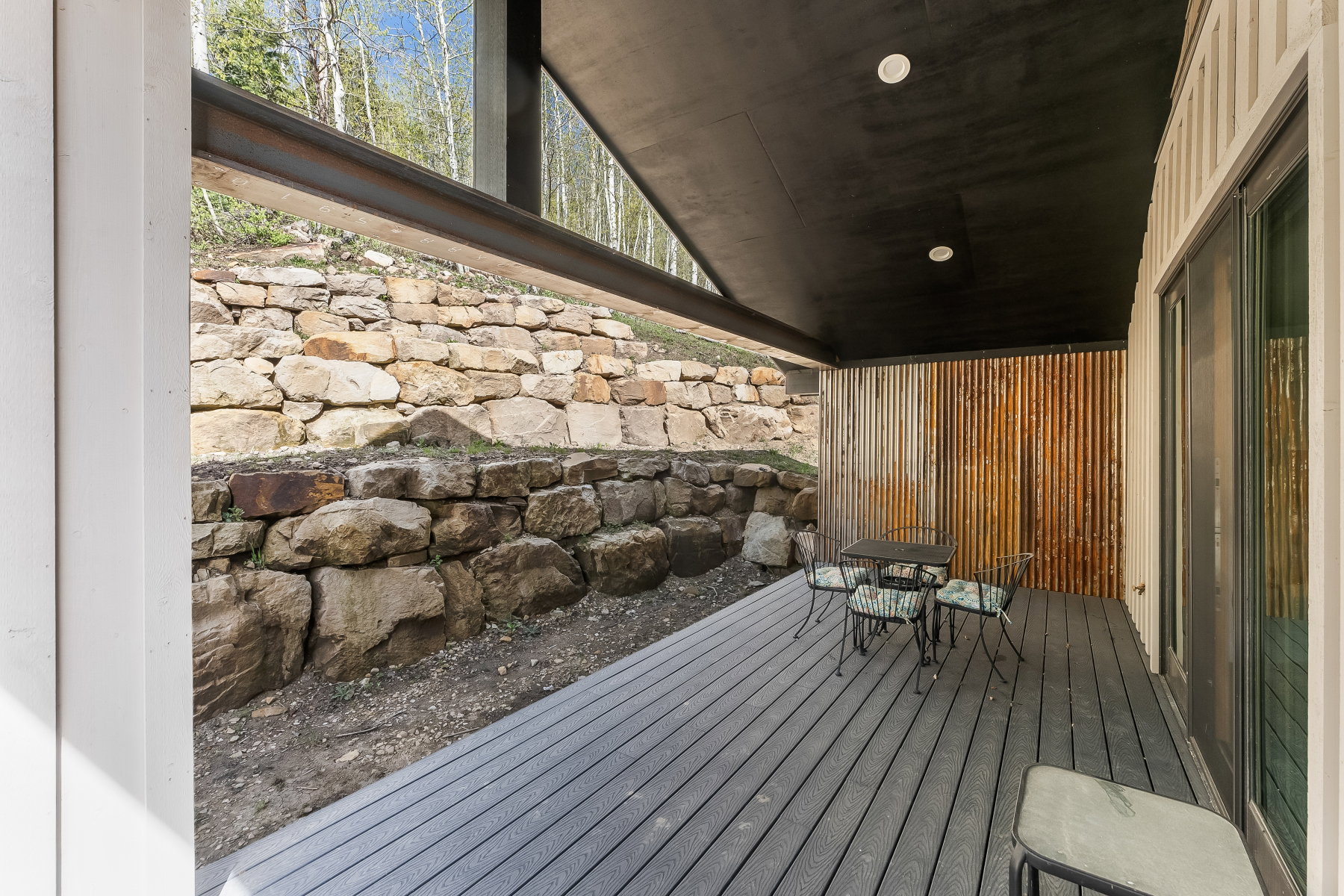 Covered outdoor patio featuring composite decking, a corrugated metal accent wall, and recessed ceiling lighting