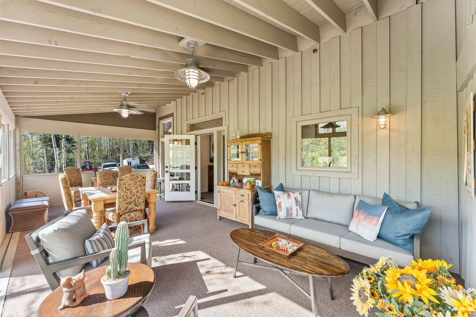 Expansive covered patio featuring a wood-plank ceiling with exposed beams, two ceiling fans, wall-mounted sconce lighting, and board-and-batten siding