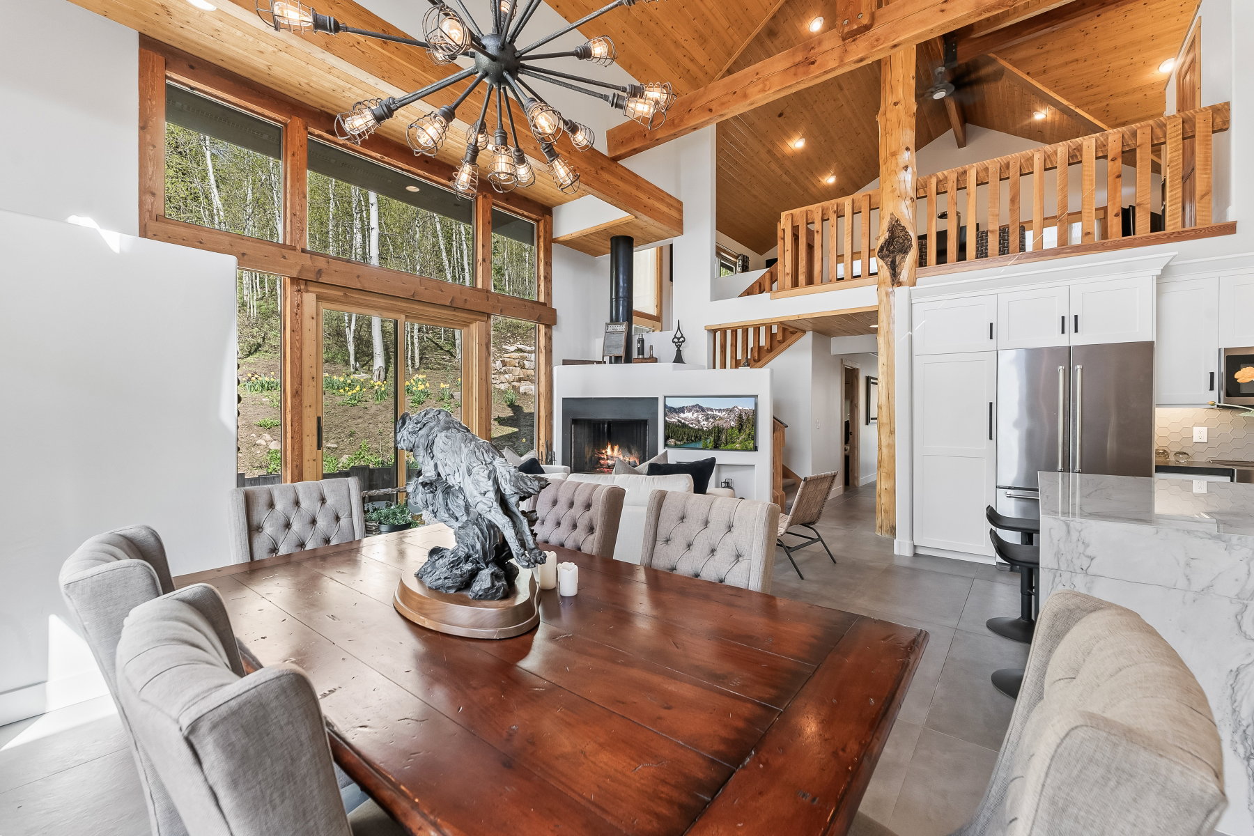 Vaulted wood-paneled ceilings with exposed beams, full-height windows, a gas fireplace, a built-in kitchen, and a lofted area