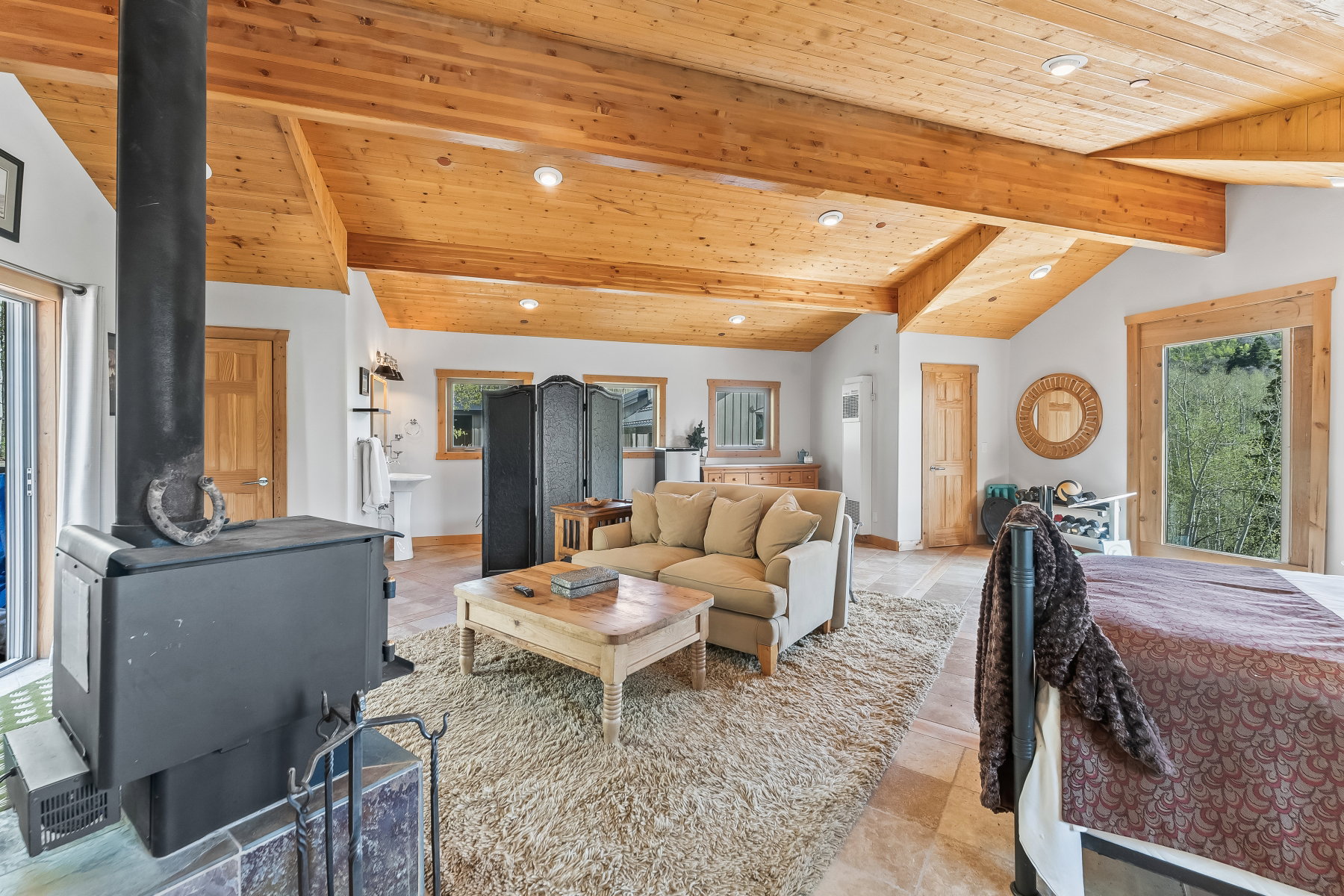 Vaulted wood-paneled ceilings with exposed beams, a built-in wood stove, and a large sliding glass door