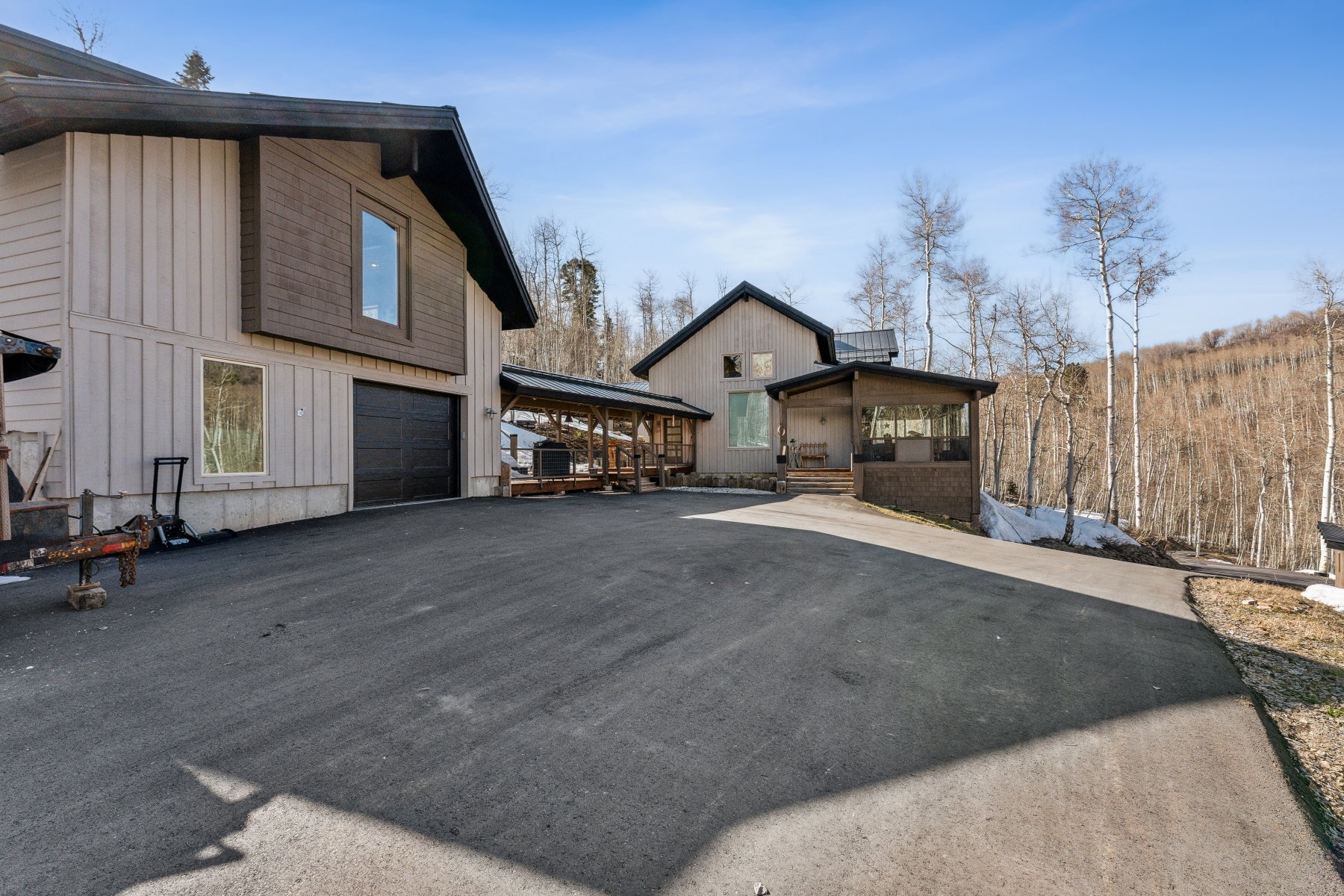 Asphalt driveway providing access to a two-story residence with a dark garage door, vertical siding, and a prominent second-story window