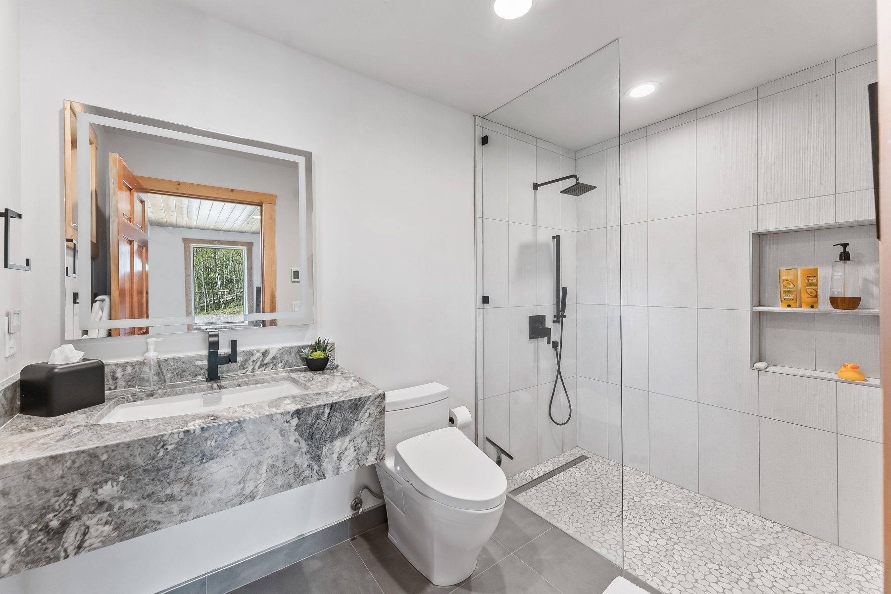 Contemporary bathroom featuring a floating vanity with a stone countertop and integrated sink, an illuminated mirror, a glass-enclosed shower with a rainfall showerhead and handheld sprayer, and a built-in shower niche