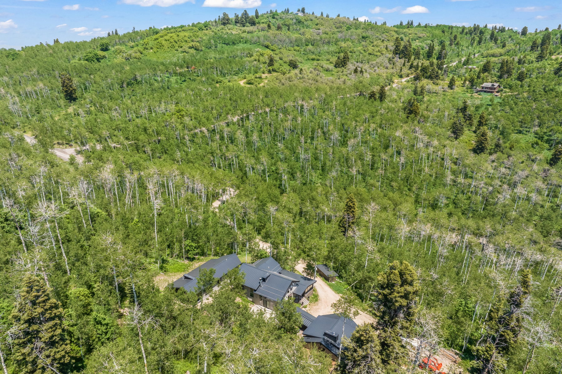 Sprawling property featuring a multi-level residence with dark roofing, surrounded by dense, varied foliage