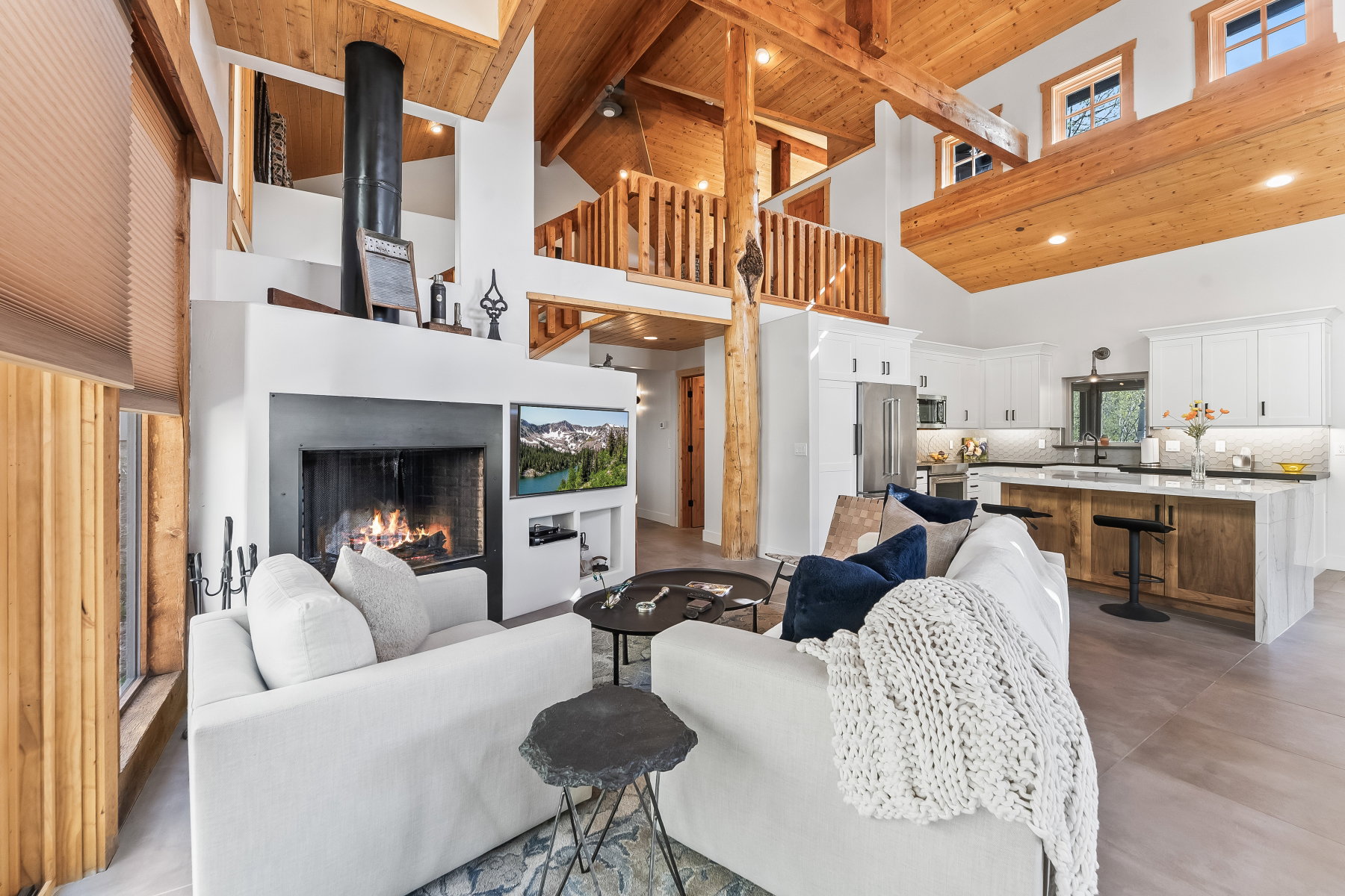 Vaulted wood-paneled ceilings with exposed beams, a white-finished fireplace with a black metal insert, and an upper-level balcony with wood railings