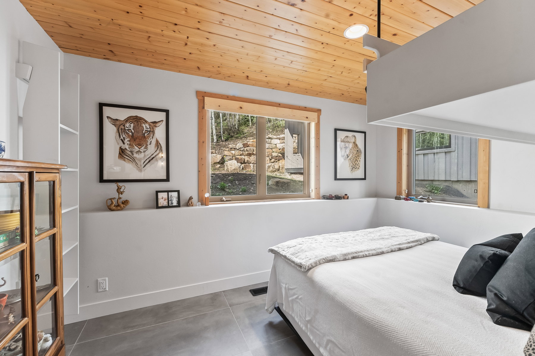 Interior room featuring a wood-finish sloped ceiling, built-in shelving, multiple windows with wood trim, and gray tile flooring