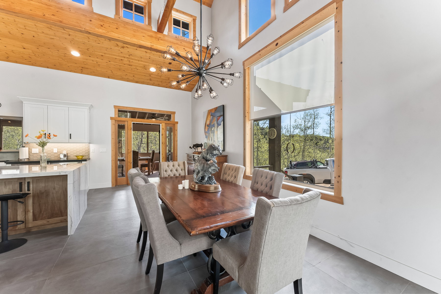 Vaulted ceilings with exposed timber beams, a modern sputnik chandelier, and a large picture window