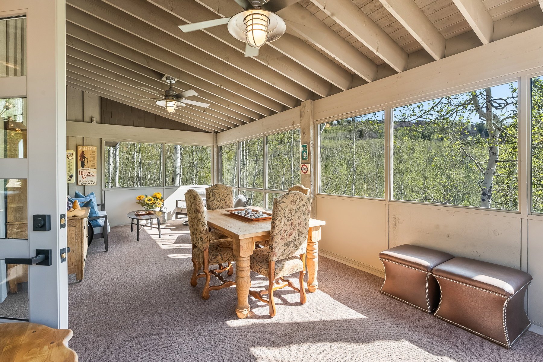 Enclosed patio featuring a vaulted wood-beam ceiling, two ceiling fans with integrated lighting, expansive windows, and light-colored carpet flooring