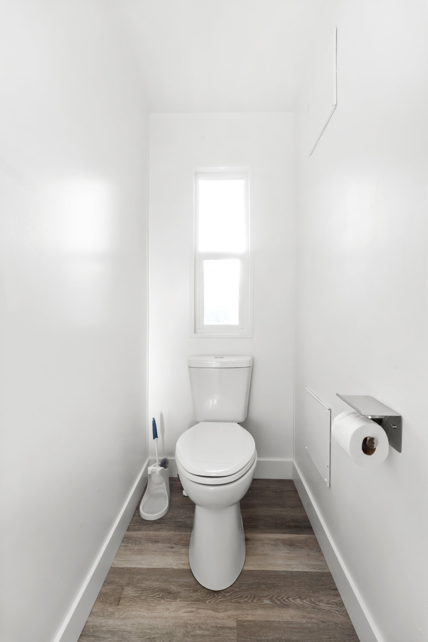Windowed water closet featuring a two-piece toilet, wood-finish flooring, white baseboards, and a wall-mounted toilet paper holder