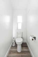 Windowed water closet featuring a two-piece toilet, wood-finish flooring, white baseboards, and a wall-mounted toilet paper holder