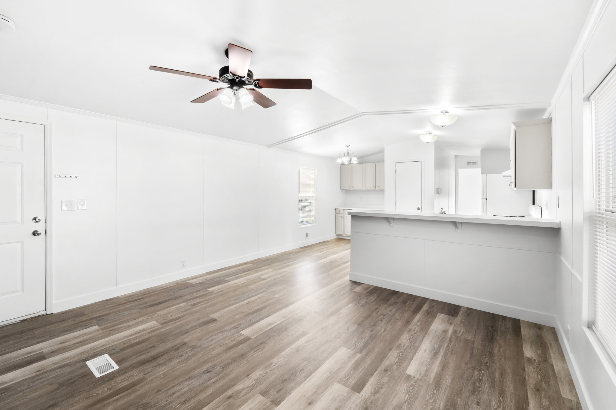 Living area featuring wood-finish flooring, white panel walls, and a ceiling fan