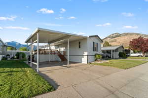 White exterior with dark shutters, featuring a covered carport and an elevated wood deck