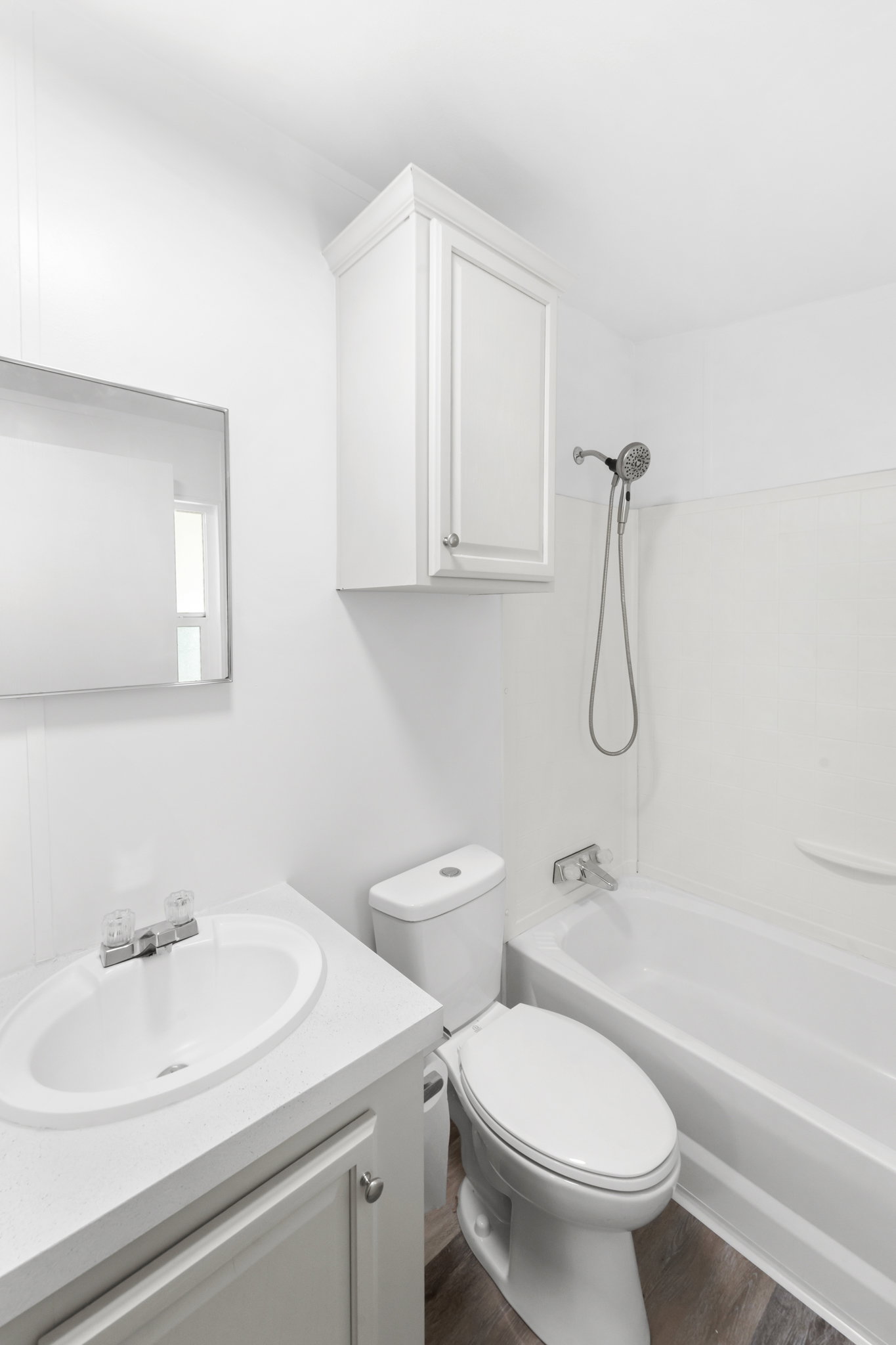 White bathroom featuring a single vanity, undermount sink, wall-mounted mirror, and white cabinetry