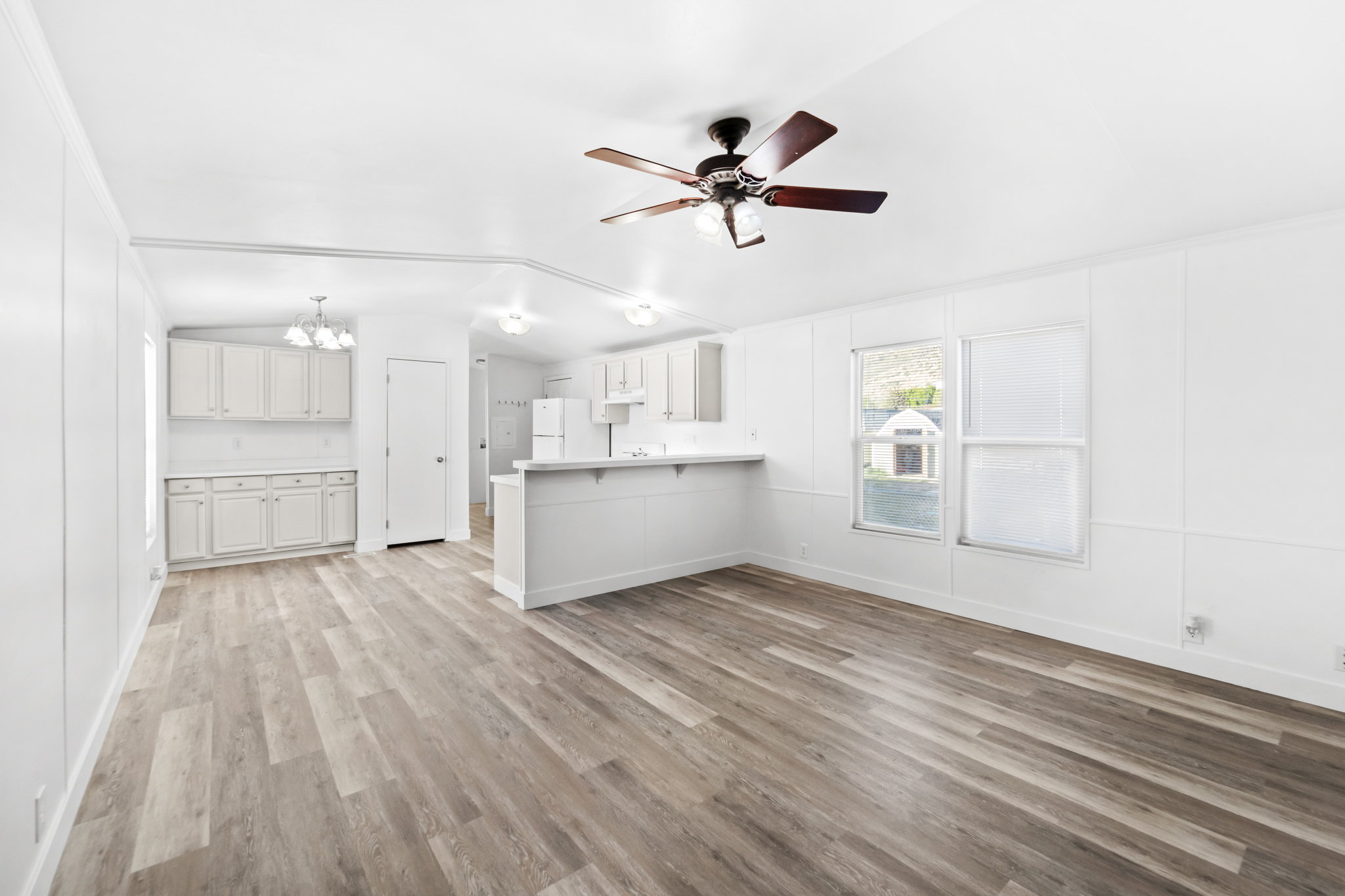Open-concept living space featuring wood-finish flooring, white panel walls, and a ceiling fan with integrated lighting