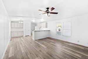 Open-concept living space featuring wood-finish flooring, white panel walls, and a ceiling fan with integrated lighting