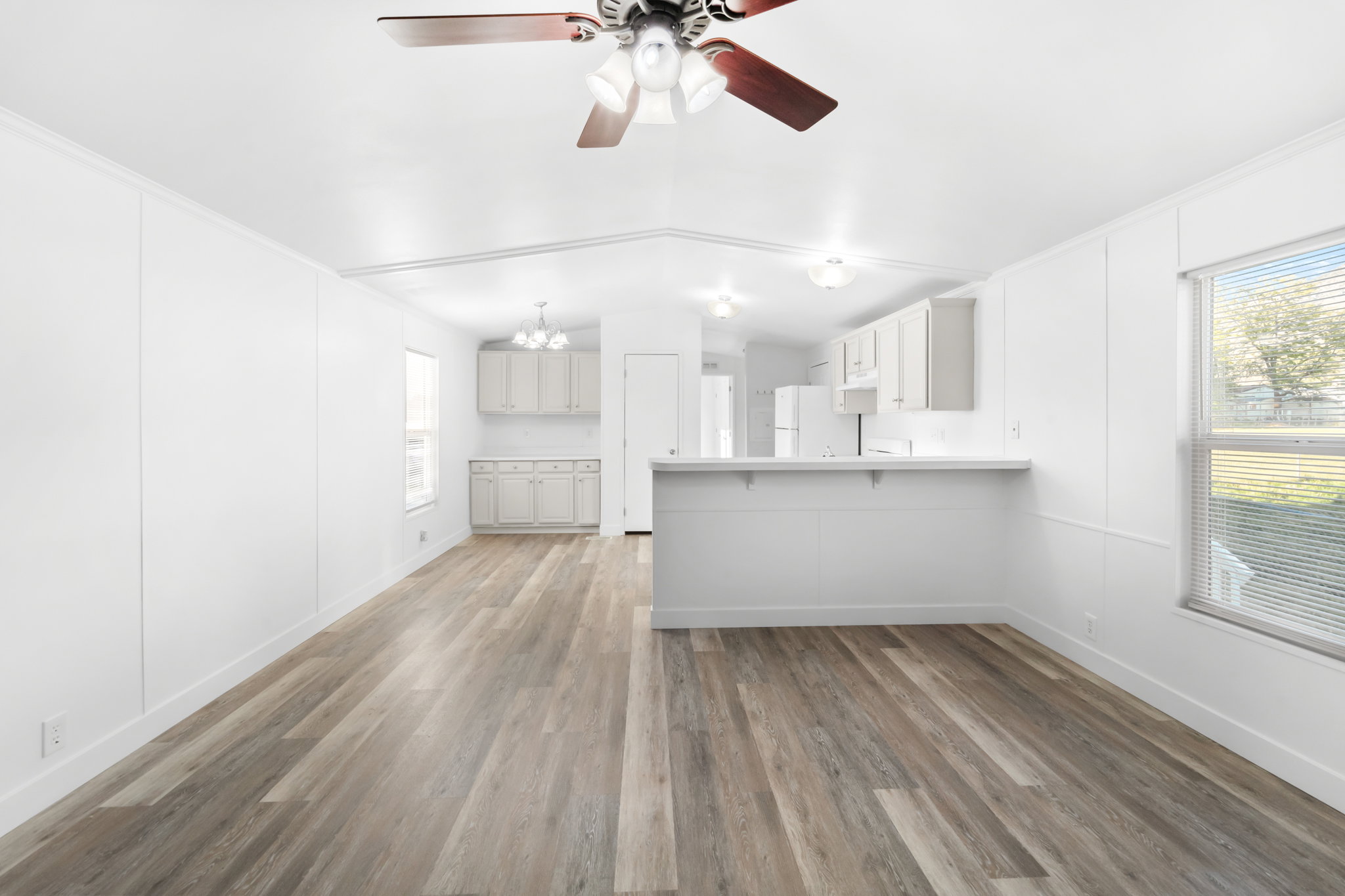 Open-concept living space featuring wood-finish flooring, white paneled walls, and a ceiling fan