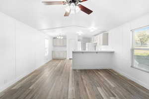 Open-concept living space featuring wood-finish flooring, white paneled walls, and a ceiling fan