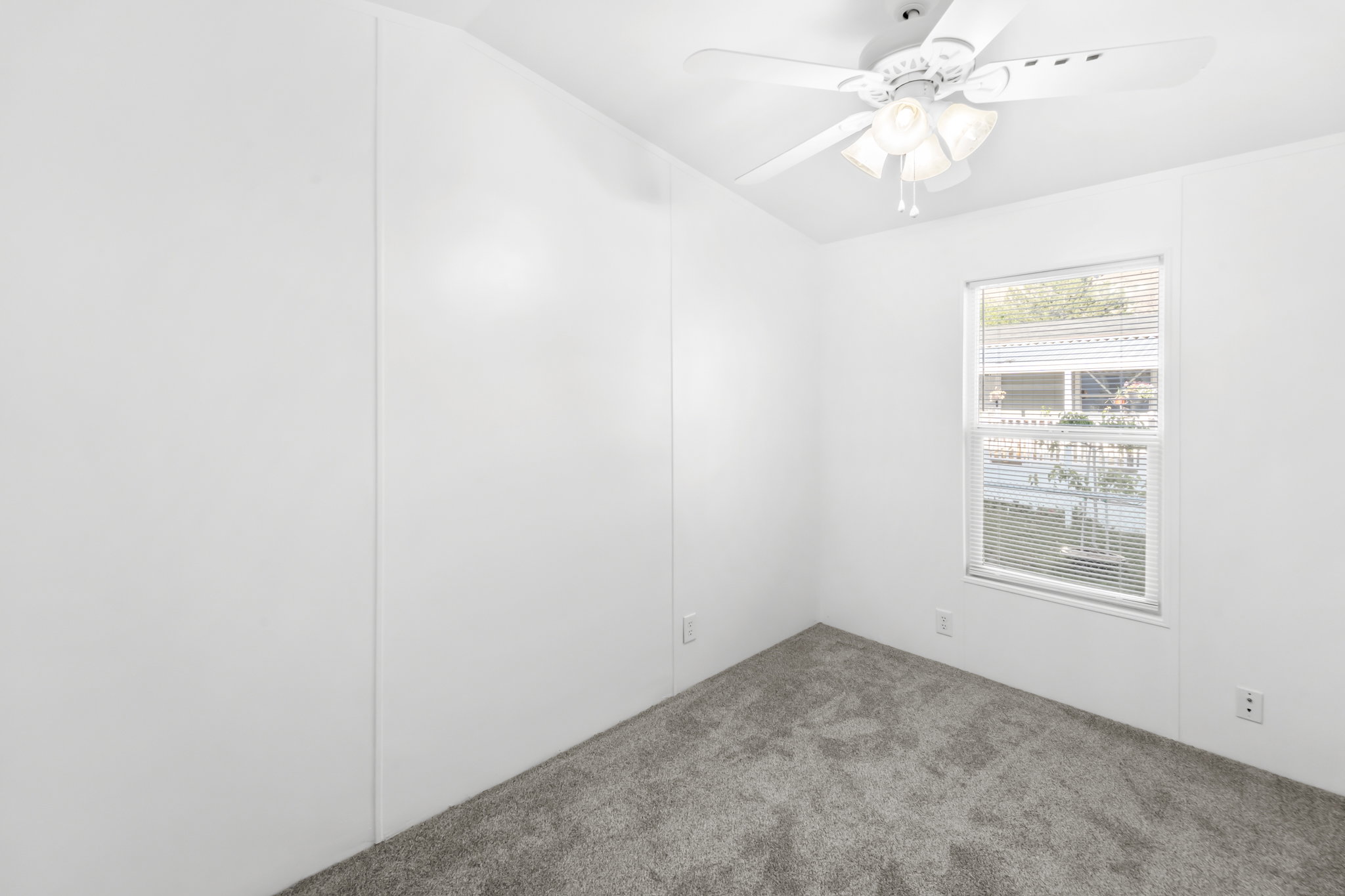 Interior room featuring light gray carpet, white walls, a white ceiling fan with integrated lighting, and a window with white blinds