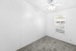 Interior room featuring light gray carpet, white walls, a white ceiling fan with integrated lighting, and a window with white blinds