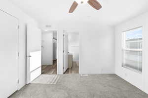 Neutral white interior featuring light gray carpeting, a window with horizontal blinds, and a ceiling fan with wood-finish blades