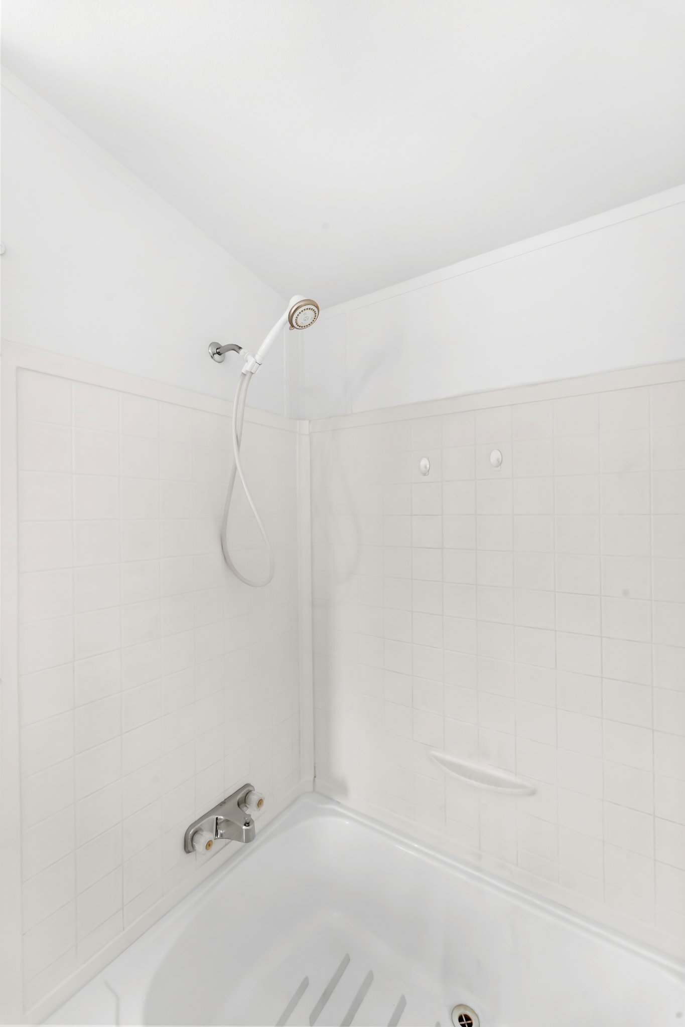 White tiled shower enclosure with a hand-held showerhead and built-in soap dishes