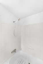 White tiled shower enclosure with a hand-held showerhead and built-in soap dishes