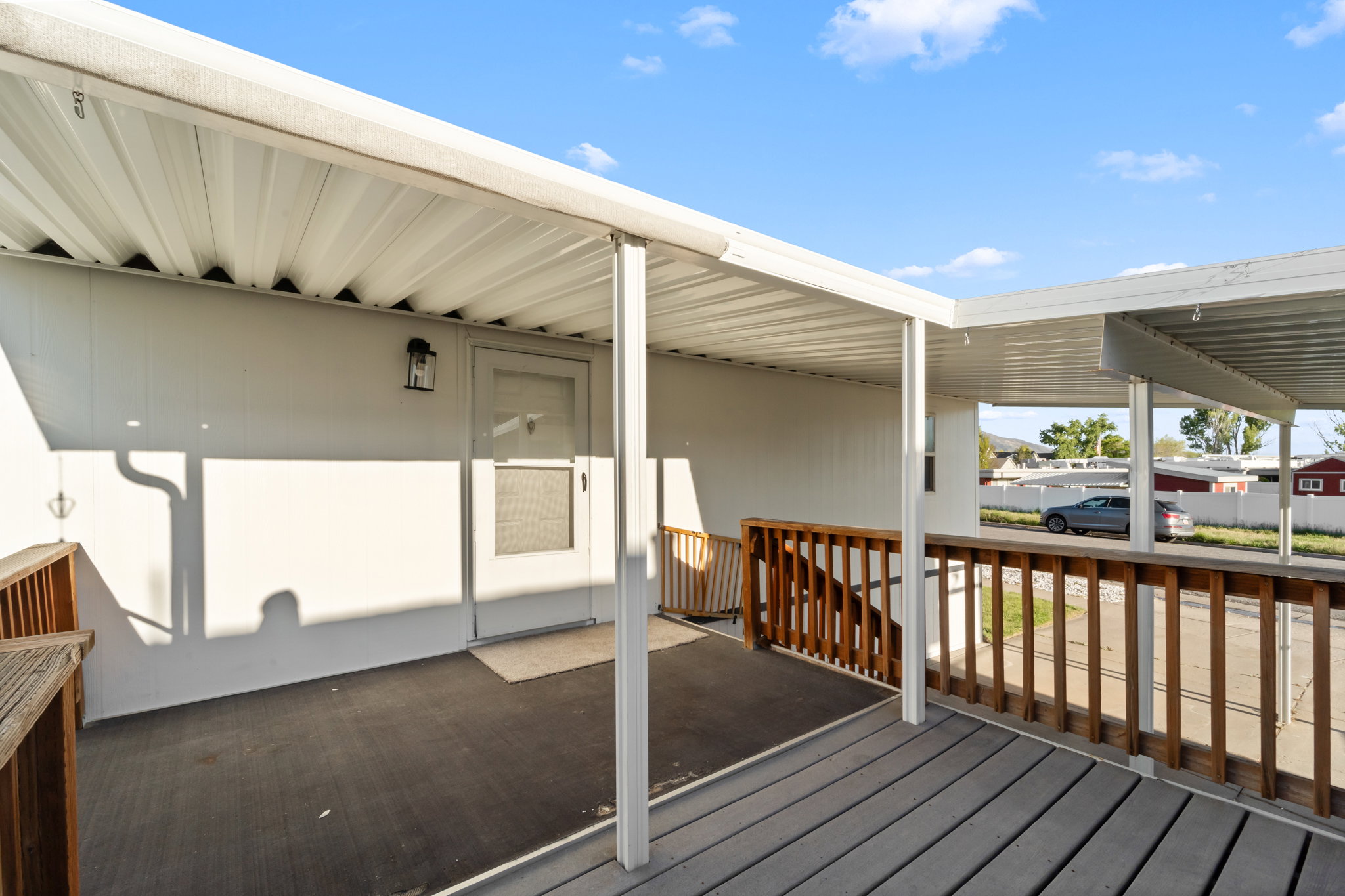 Covered porch with wood railing, featuring a solid exterior door and exterior wall sconce