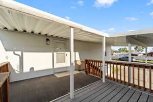 Covered porch with wood railing, featuring a solid exterior door and exterior wall sconce