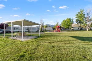 Expansive green space featuring a covered picnic area with a concrete pad and a playground structure