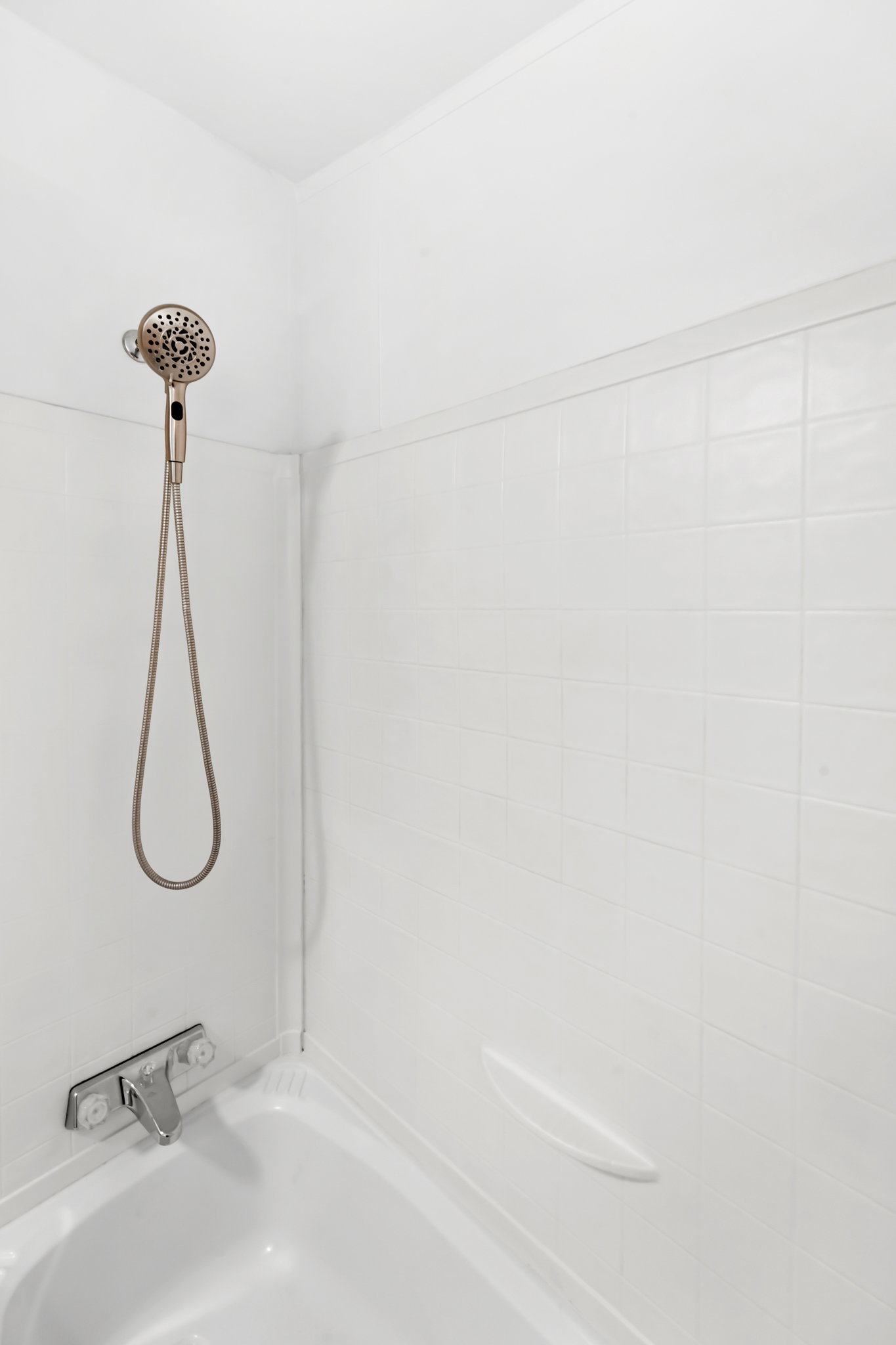 Bathtub and shower combination featuring white tiled walls and a handheld shower fixture