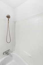 Bathtub and shower combination featuring white tiled walls and a handheld shower fixture
