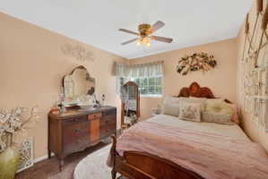 Bedroom featuring a ceiling fan with integrated lighting, wood-finish headboard, and window with blinds