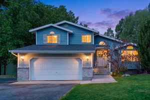Split-level residence featuring a two-car garage, stone accent siding, and multiple arched windows