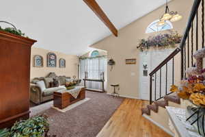 Vaulted ceiling living area with a decorative wood beam, carpet flooring, and a front entry featuring an arched transom window