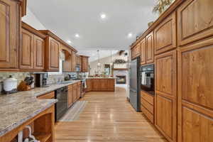 Expansive kitchen featuring abundant wood cabinetry, integrated stainless steel appliances, speckled countertops, and wood-finish flooring