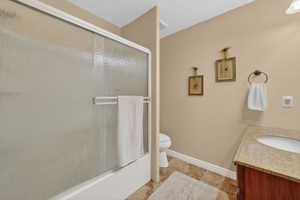 Shower/tub combination with textured glass sliding doors, a vanity with a stone-look countertop, a built-in sink, and tile flooring