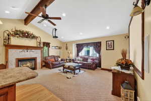Vaulted ceiling living area featuring a stone-surround fireplace with a wood mantle, exposed wood beam, ceiling fan, and recessed lighting
