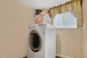 Dedicated laundry area featuring a front-load washing machine, neutral-toned walls, and a window with blinds