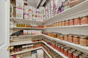 Well-organized pantry featuring extensive built-in shelving, white painted walls, and a solid white door with a brass-finish doorknob