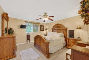 Carpeted bedroom featuring a window with blinds, a ceiling fan with light fixture, and crown molding